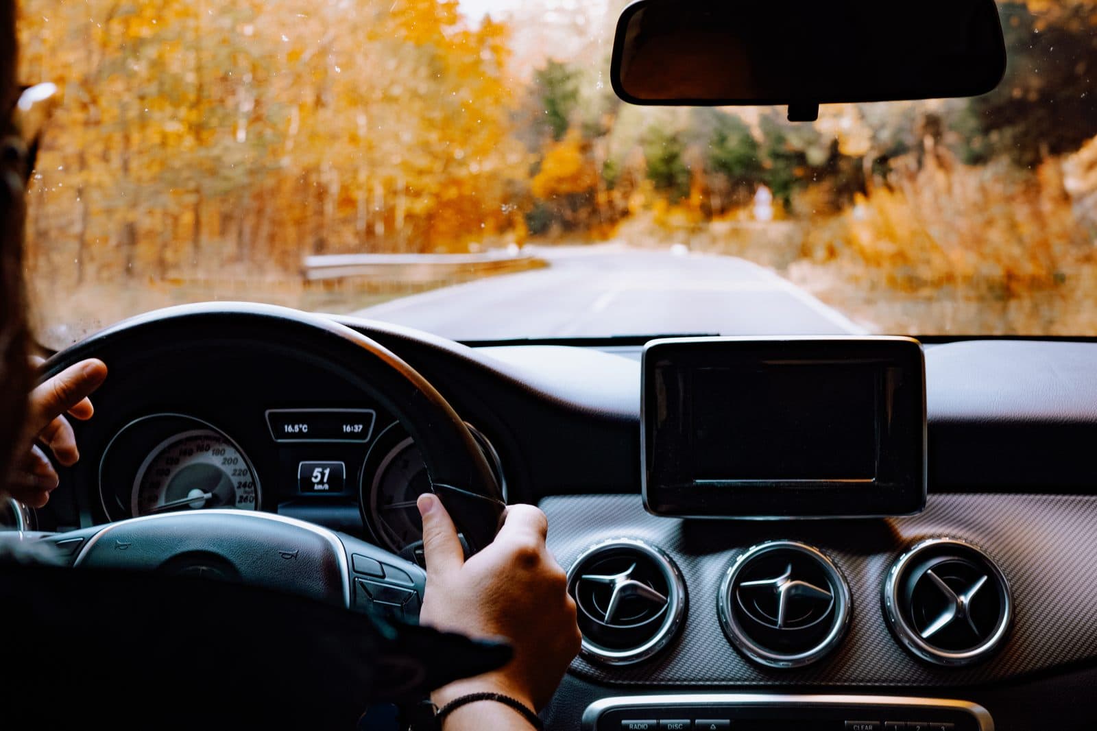 Driver's point of view gripping the steering wheel on an autumn road